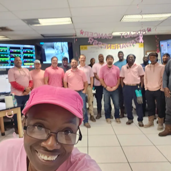 Sandra Myers smiles for a selfie in a pink cap and shirt, with Pulp Mill coworkers wearing pink behind her.
