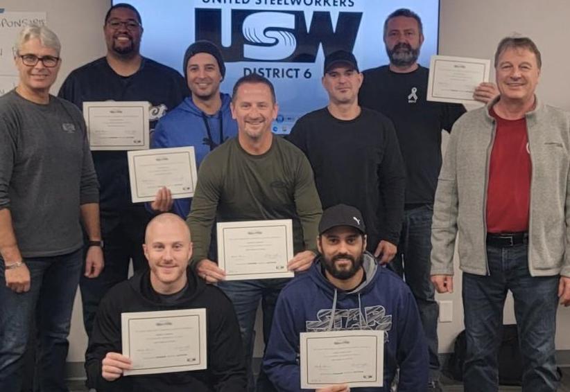 Union executives holding their certificates standing in front of the USW logo